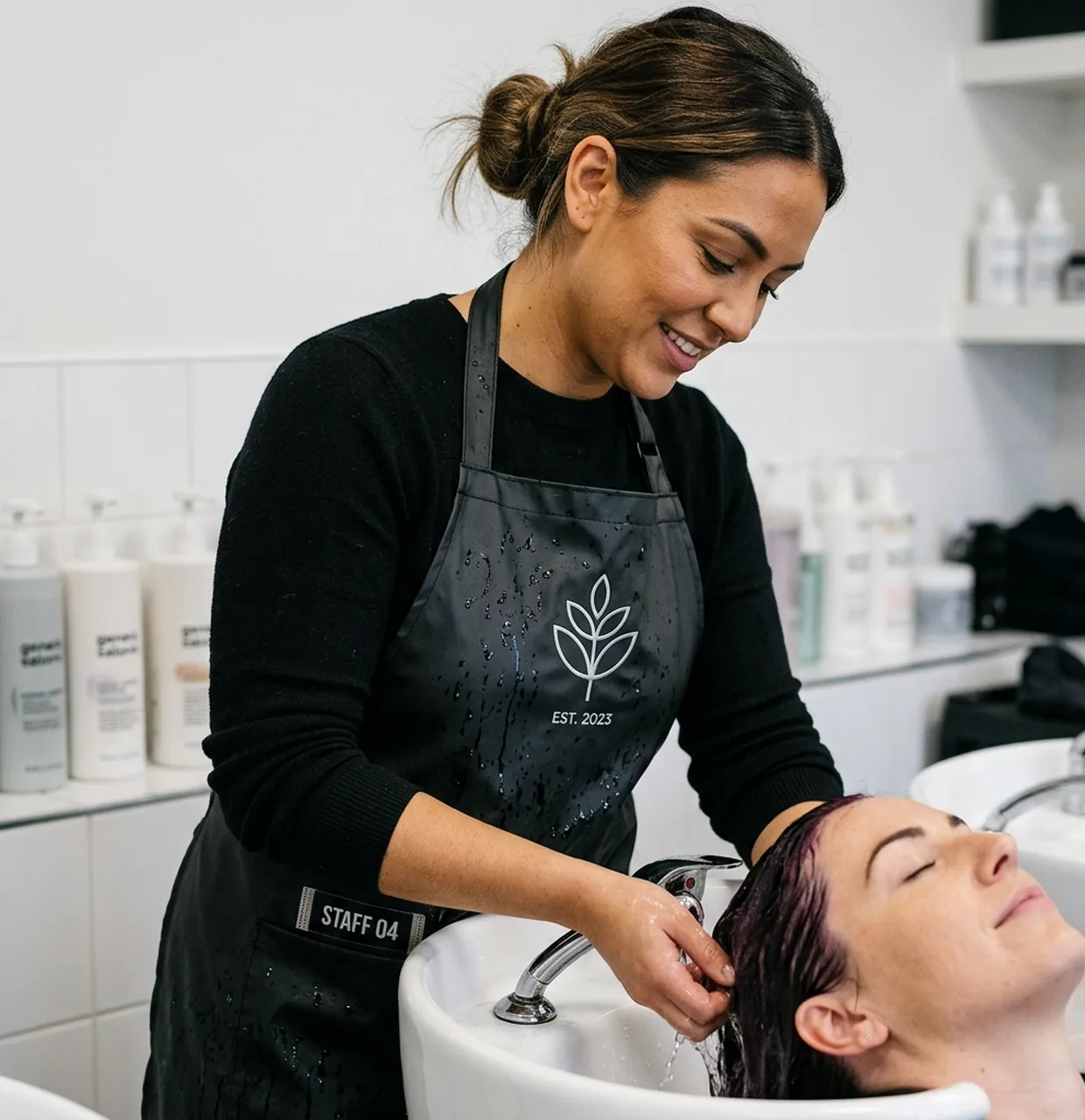 Colourist at the basin wearing a coated stylist apron while rinsing colour