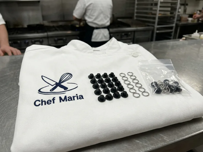 Removable stud buttons with ring clips beside a small bag on a folded chef coat