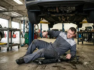 Technician on a creeper sliding out from under a car, back and seat of the coverall on the board