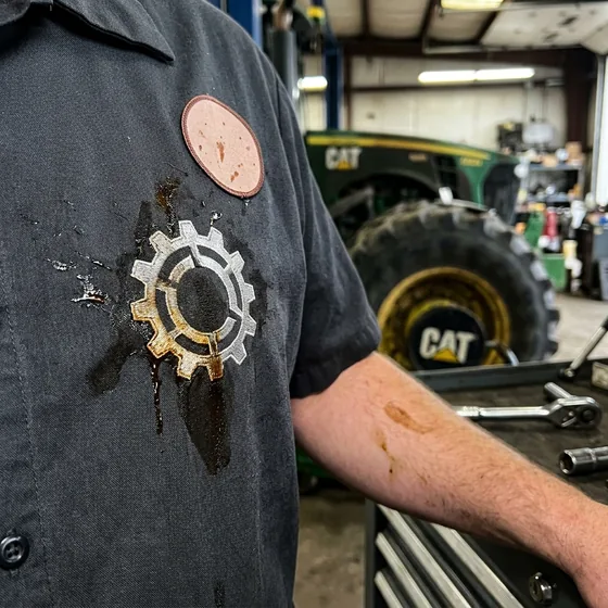 Close-up of a splash of brake fluid across a wordless embroidered chest logo on a work shirt