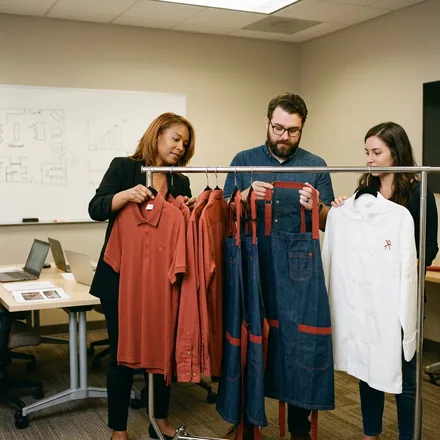 Brand HQ operations team reviewing a rail of approved sample uniforms in a training room