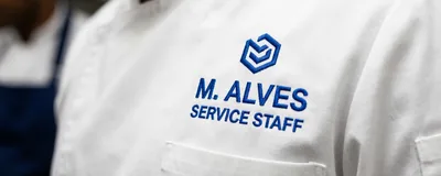 An embroidered employee name under the logo on a white chef coat